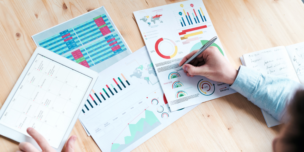 Man writing down on a bar chart and pie graph on a wooden table