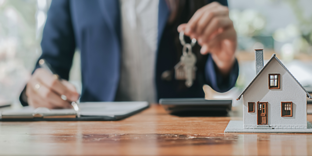 Person holding up a set of keys next to a house