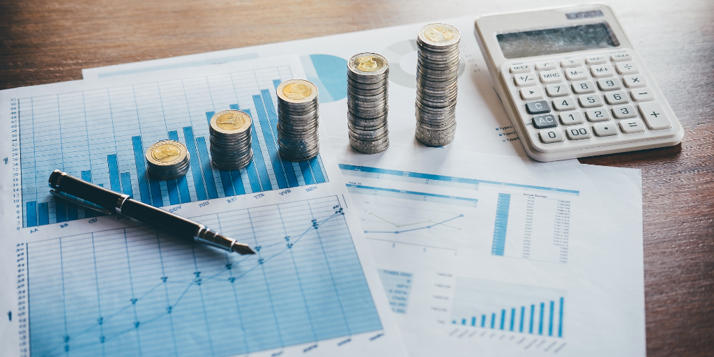 Coins stacked next to a calculator placed on top of a bar chart