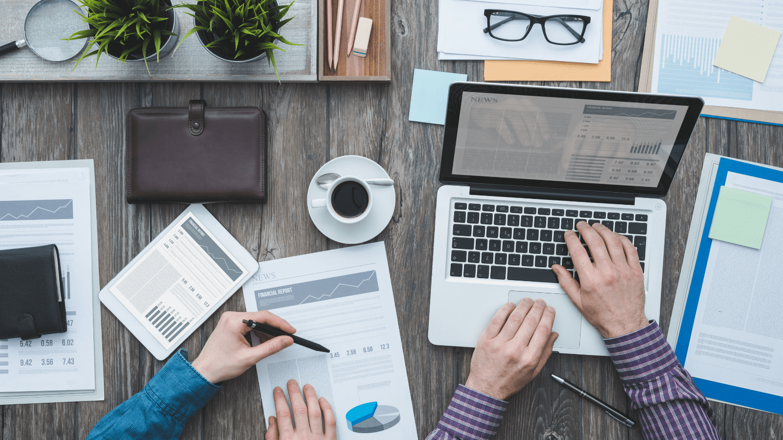 Two people sat at a desk with pen and paper plus a laptop working