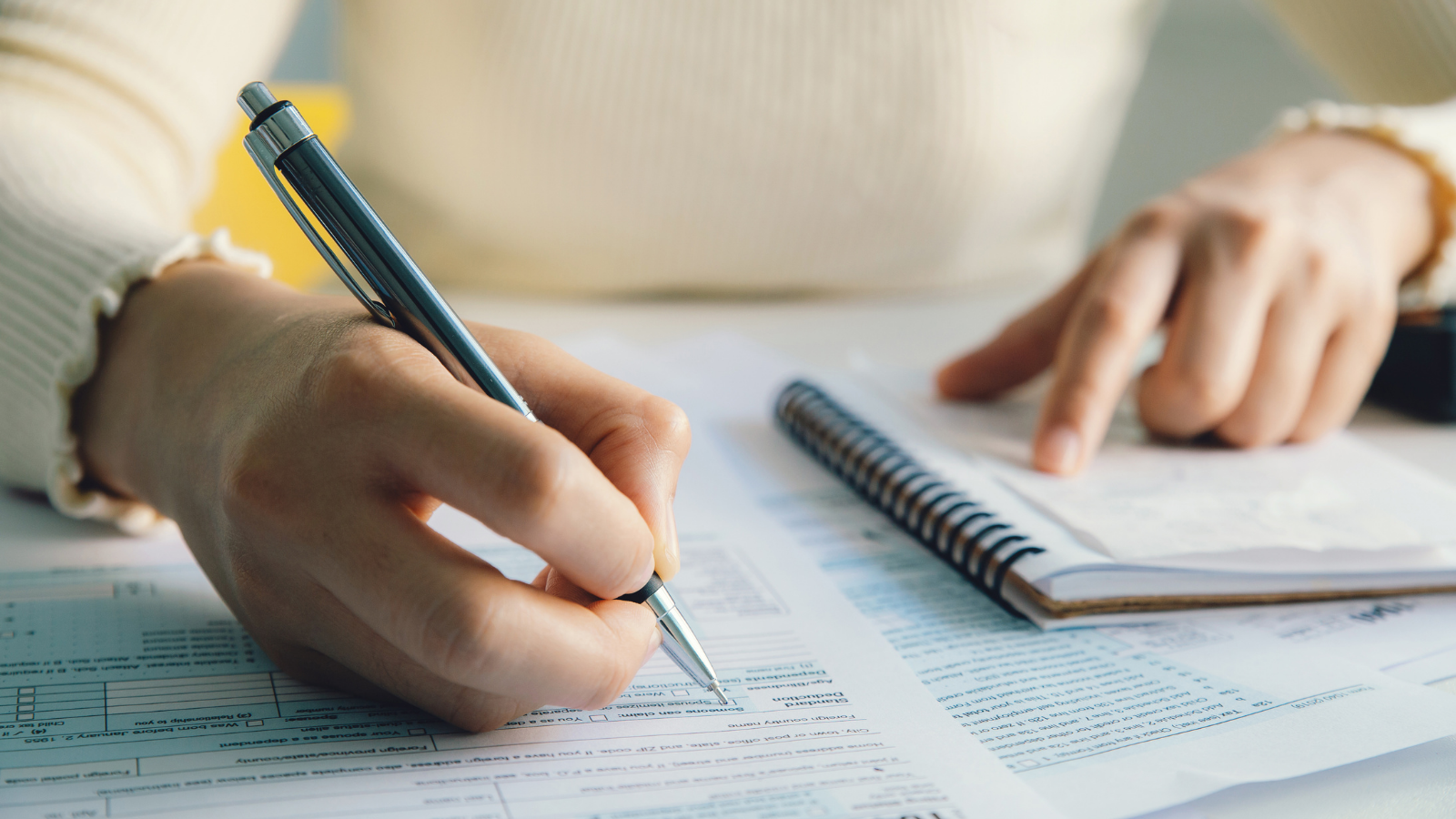 Women writing on a piece of paper whilst pointing at a notebook